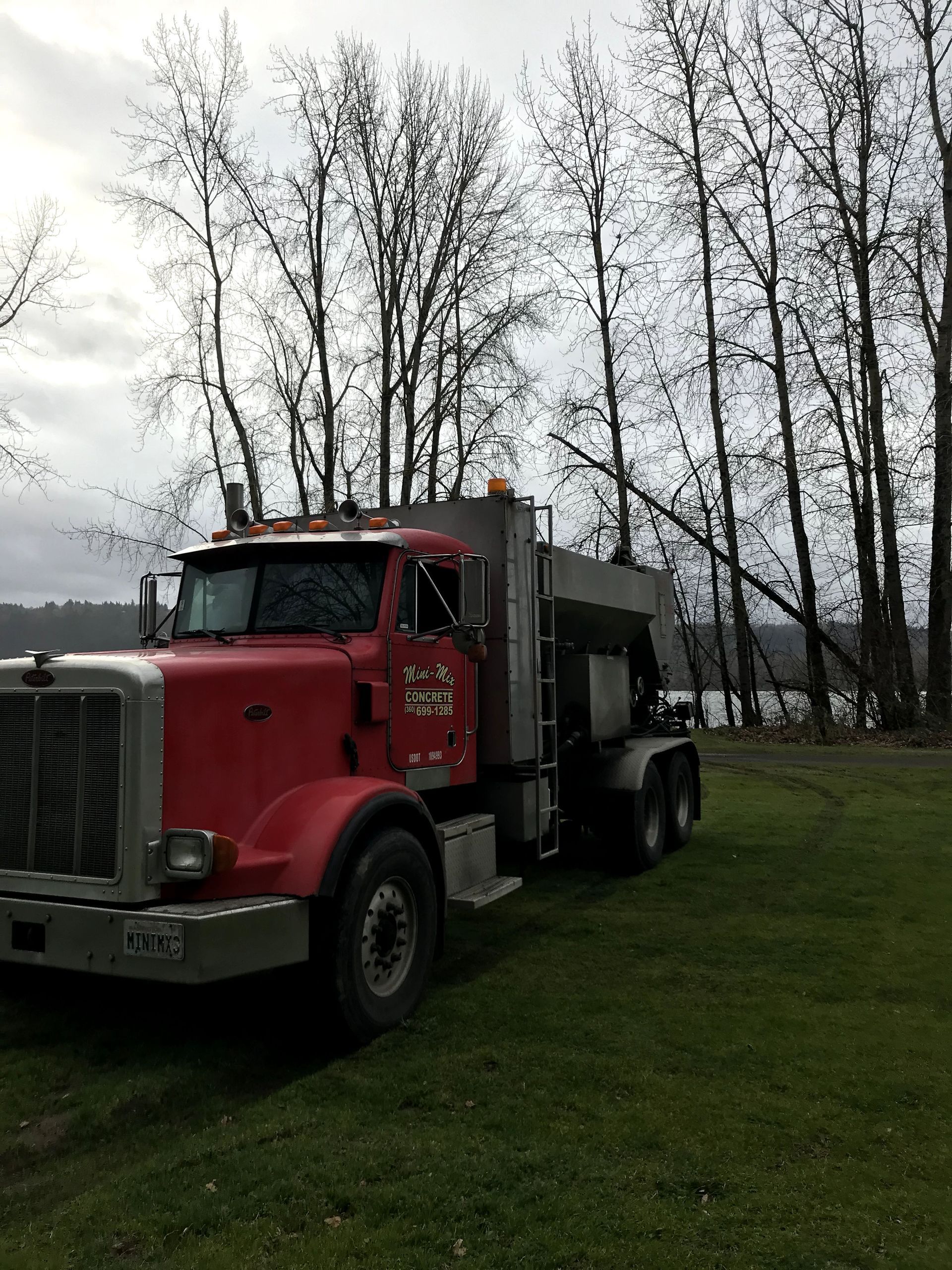 A red semi truck is parked in a grassy field with trees in the background.