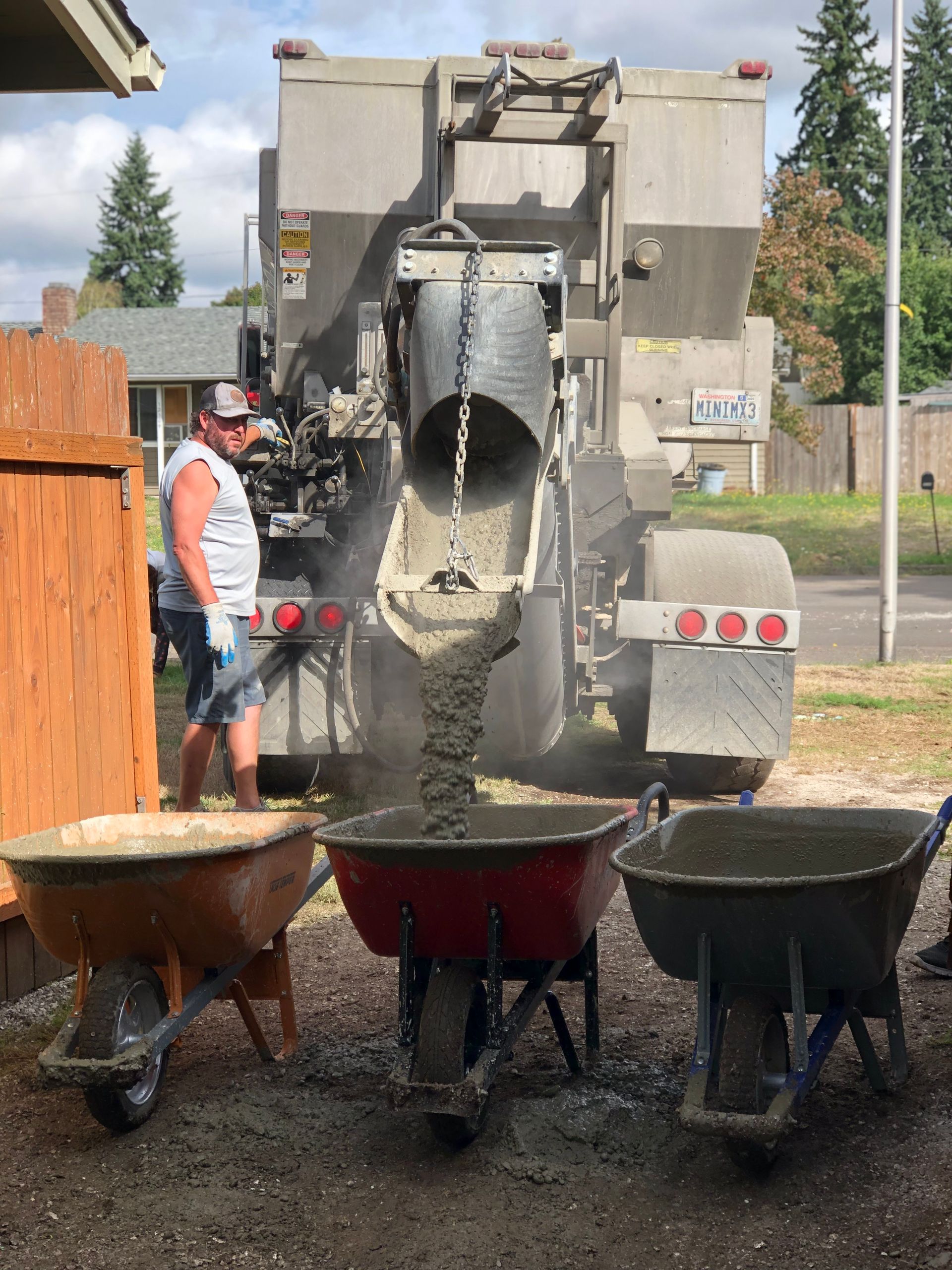 A man is pouring concrete into wheelbarrows in front of a concrete truck.