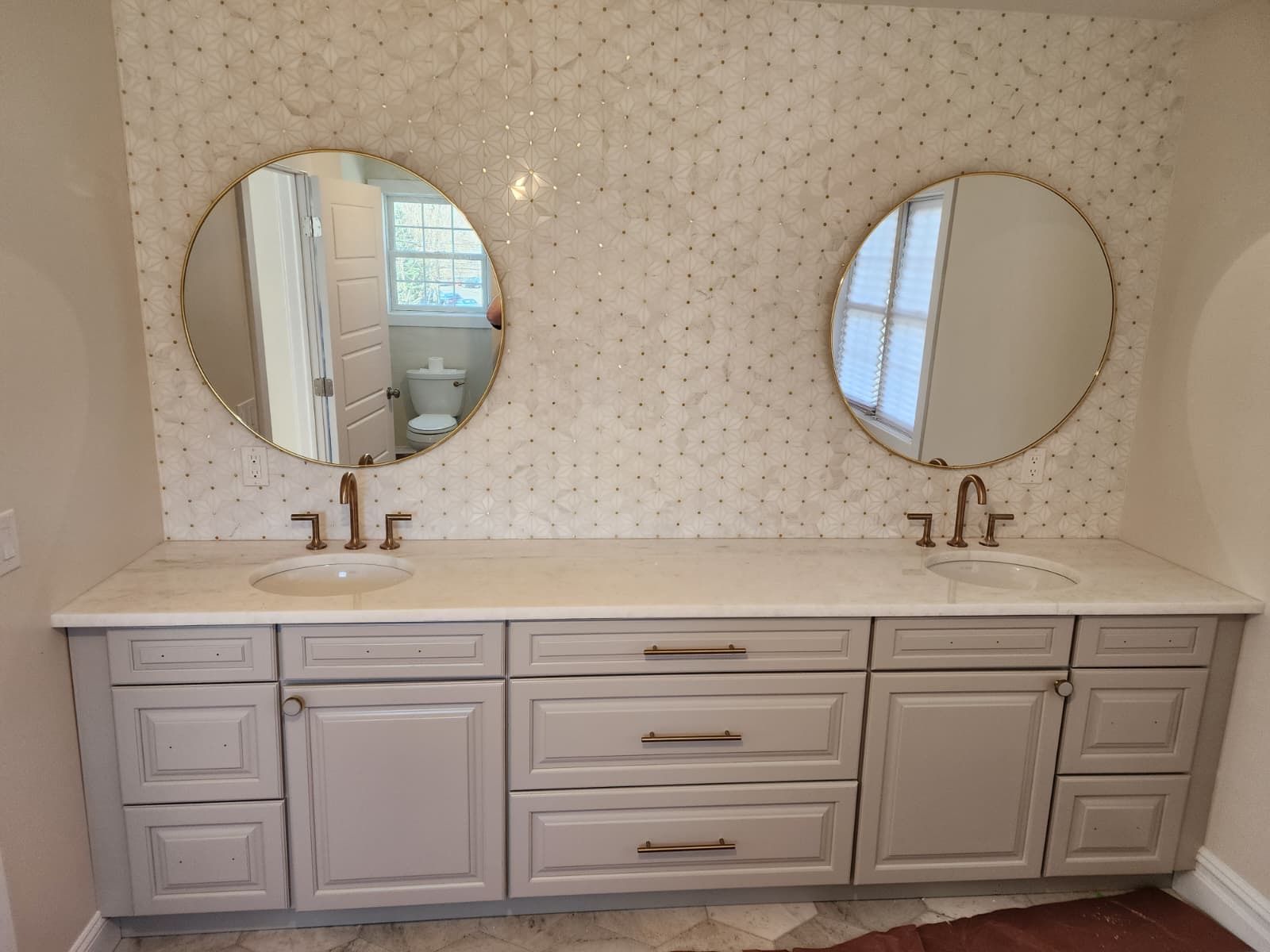 Double bathroom vanity with white countertop, two round mirrors, and gray cabinetry against a patterned mosaic wall.