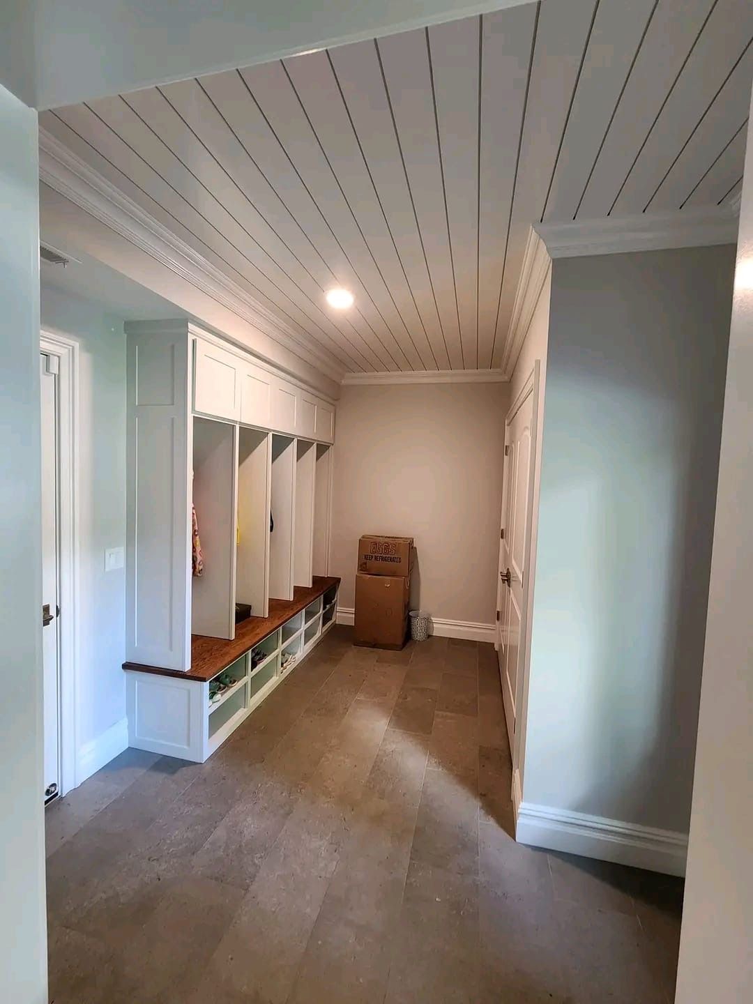 A bright mudroom with white built-in lockers, a wooden bench, shiplap ceiling, and light gray walls.