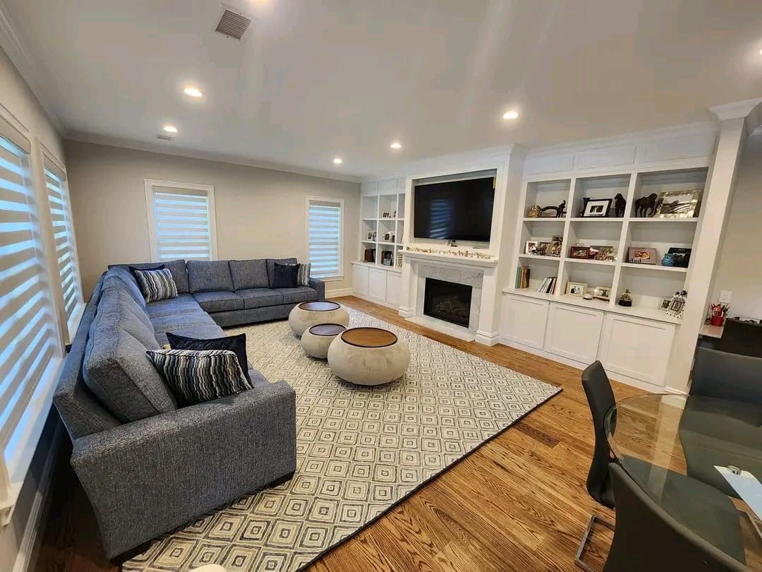 A spacious living room with a large gray sectional sofa, patterned rug, fireplace, and built-in white bookshelves.