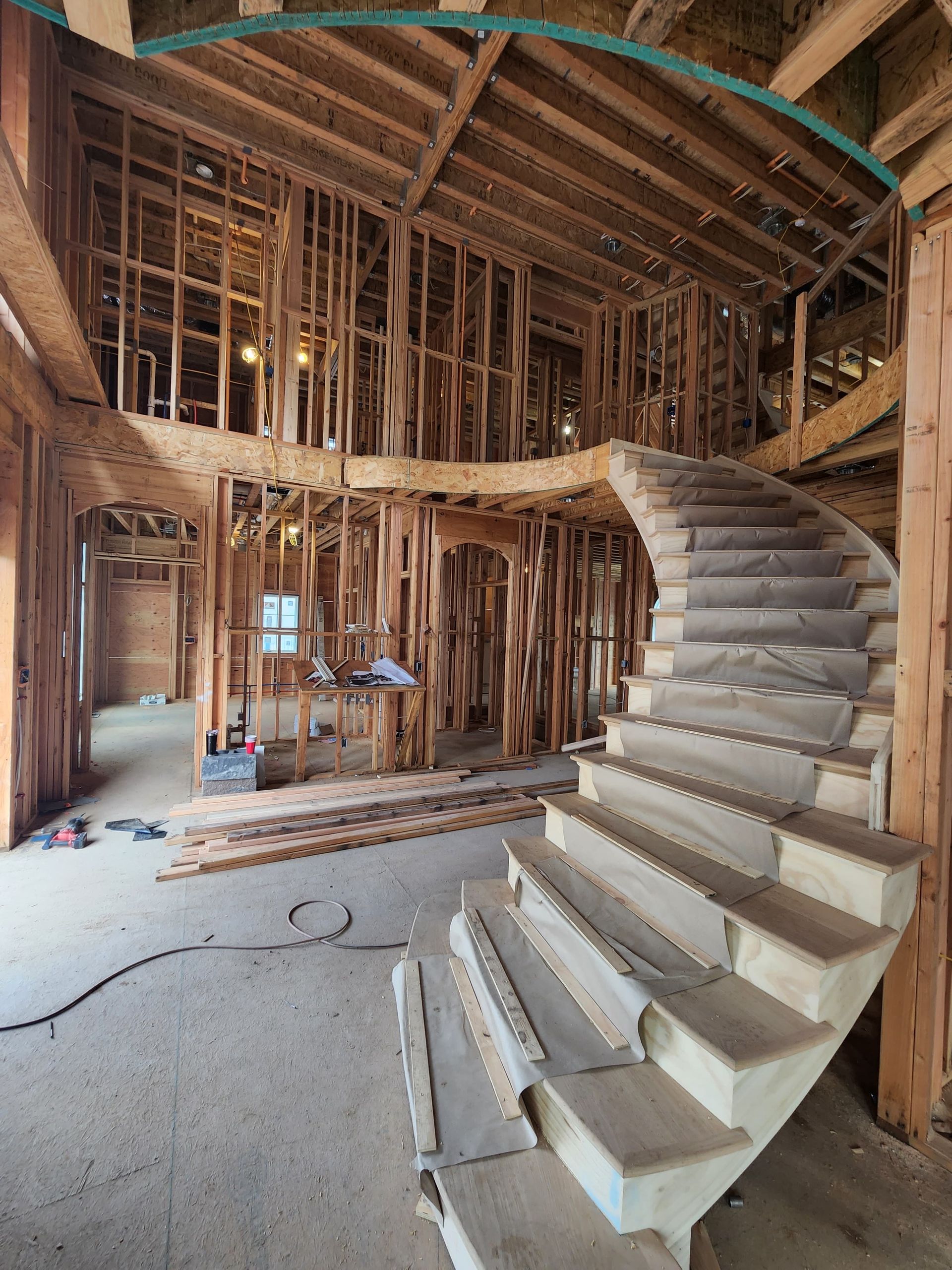 A curved staircase stands in the foreground of a residential construction site with exposed wooden framing and joists.