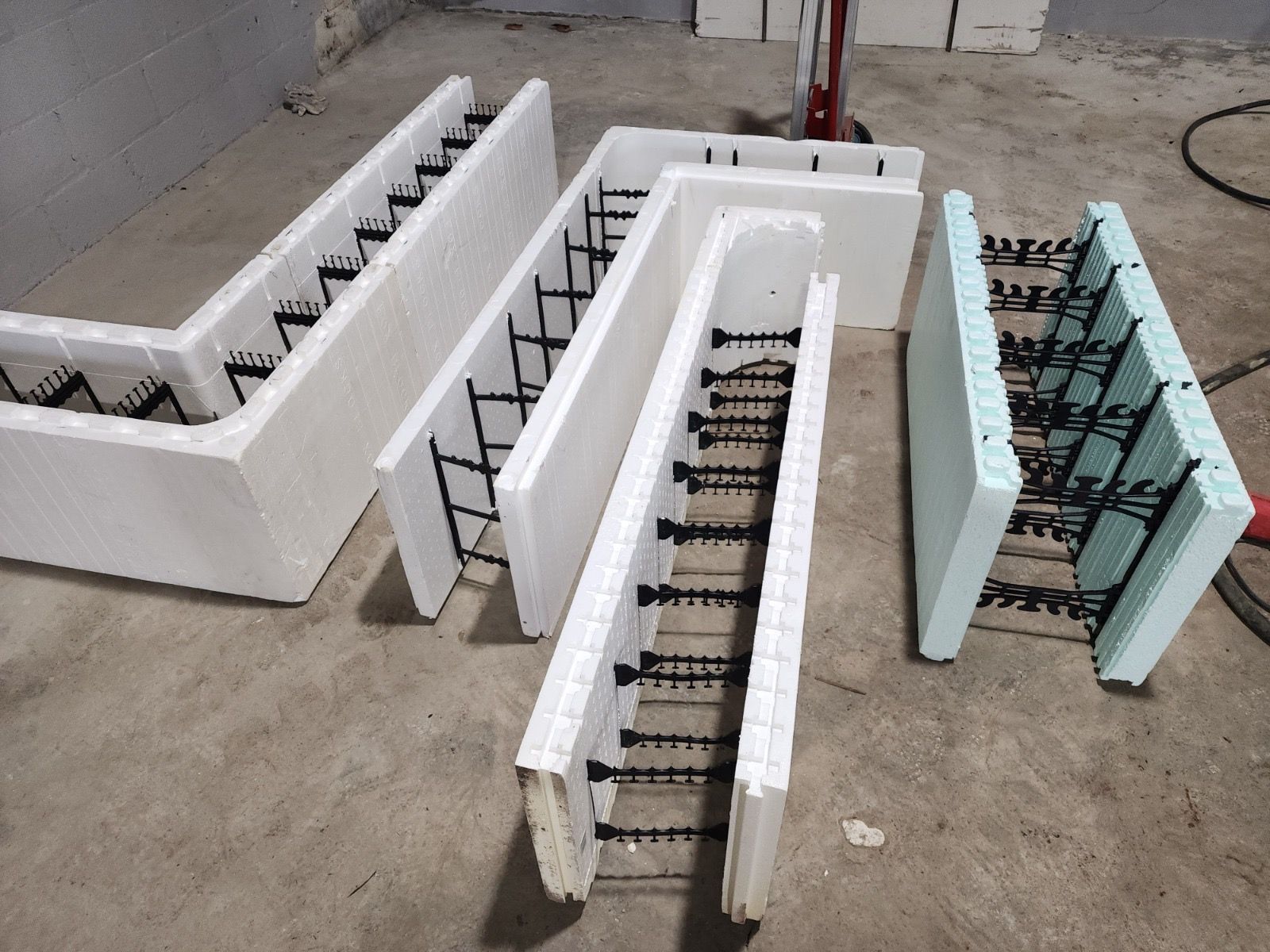 Several white and light blue insulated concrete form blocks with black plastic connectors, arranged on a concrete floor.