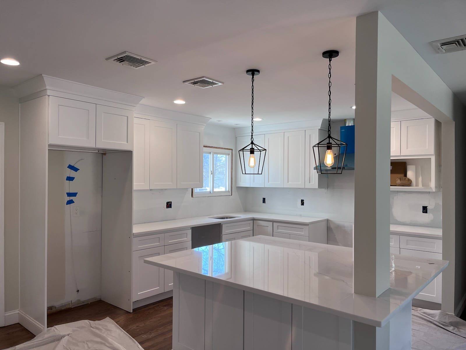 A modern white kitchen featuring a central island, shaker-style cabinets, quartz countertops, and hanging pendant lights.
