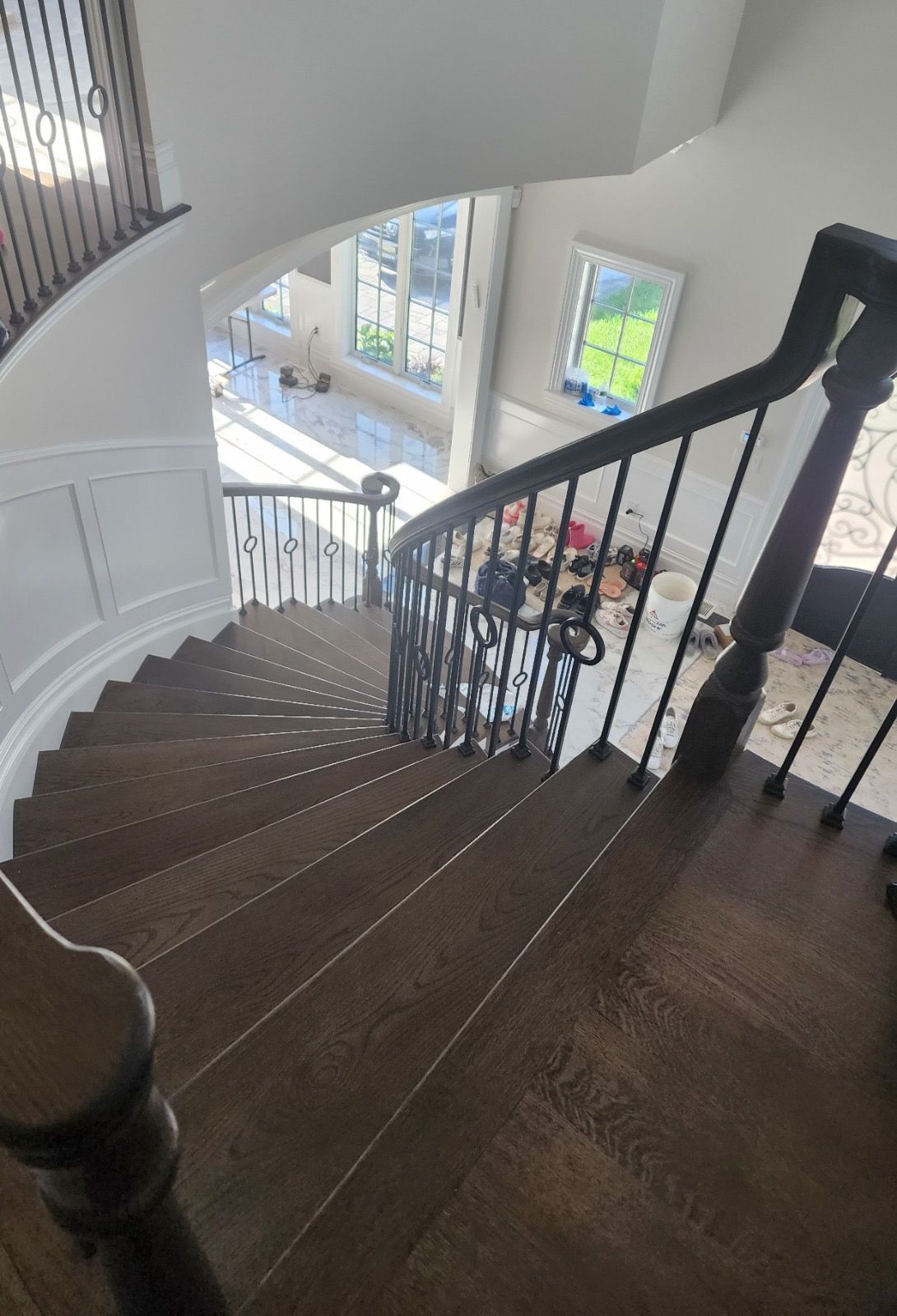 A high-angle view looking down a curved staircase with dark wooden steps, black railings, and white paneling.