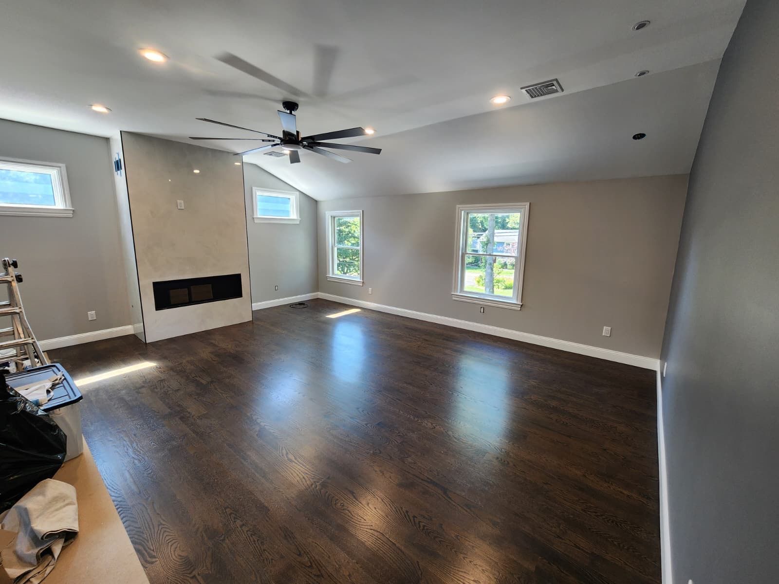 A spacious living room featuring dark wood floors, light grey walls, a modern fireplace, and large windows.