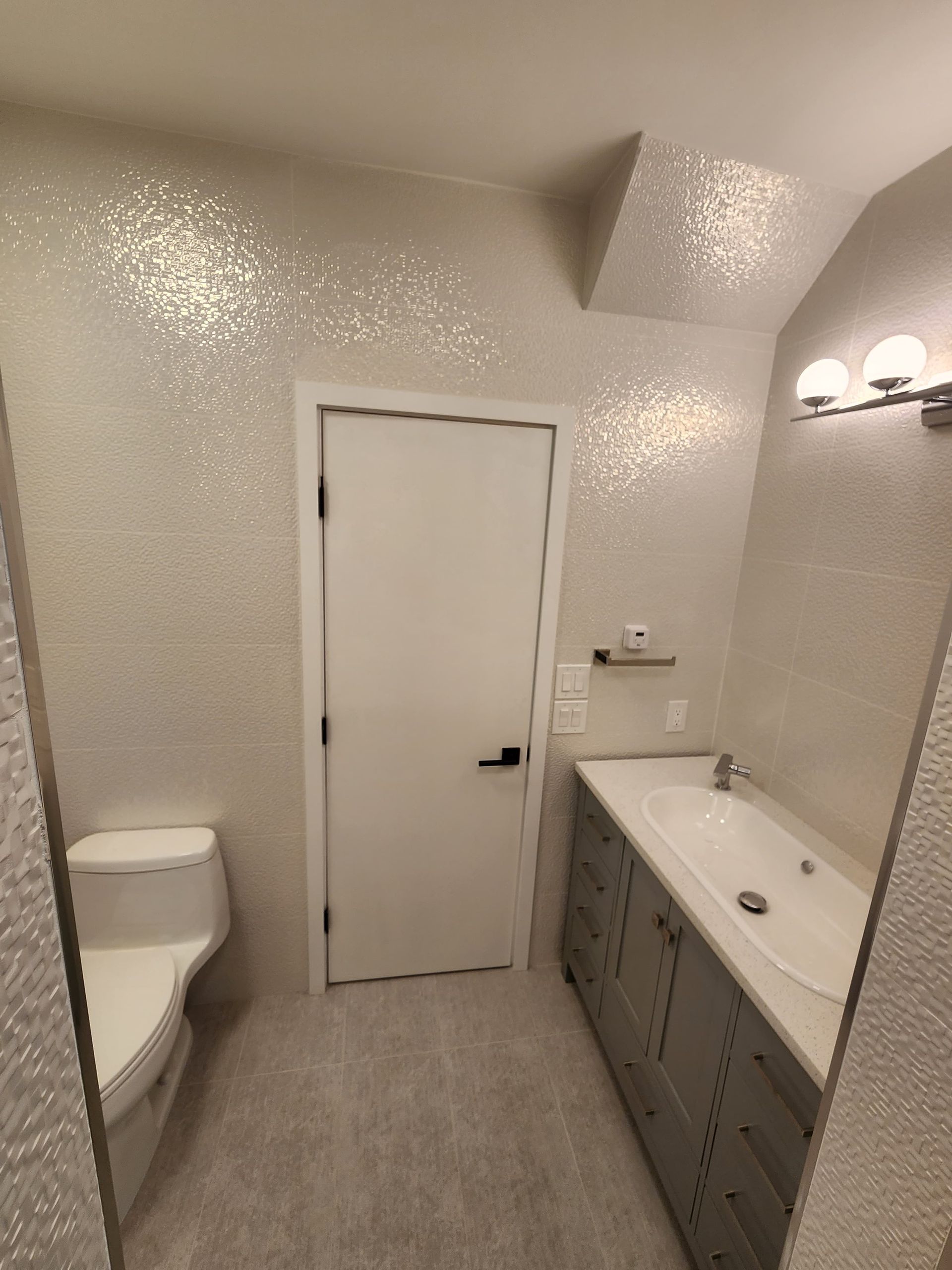 A bathroom with a grey vanity, a white toilet, and textured, silver-flecked walls.