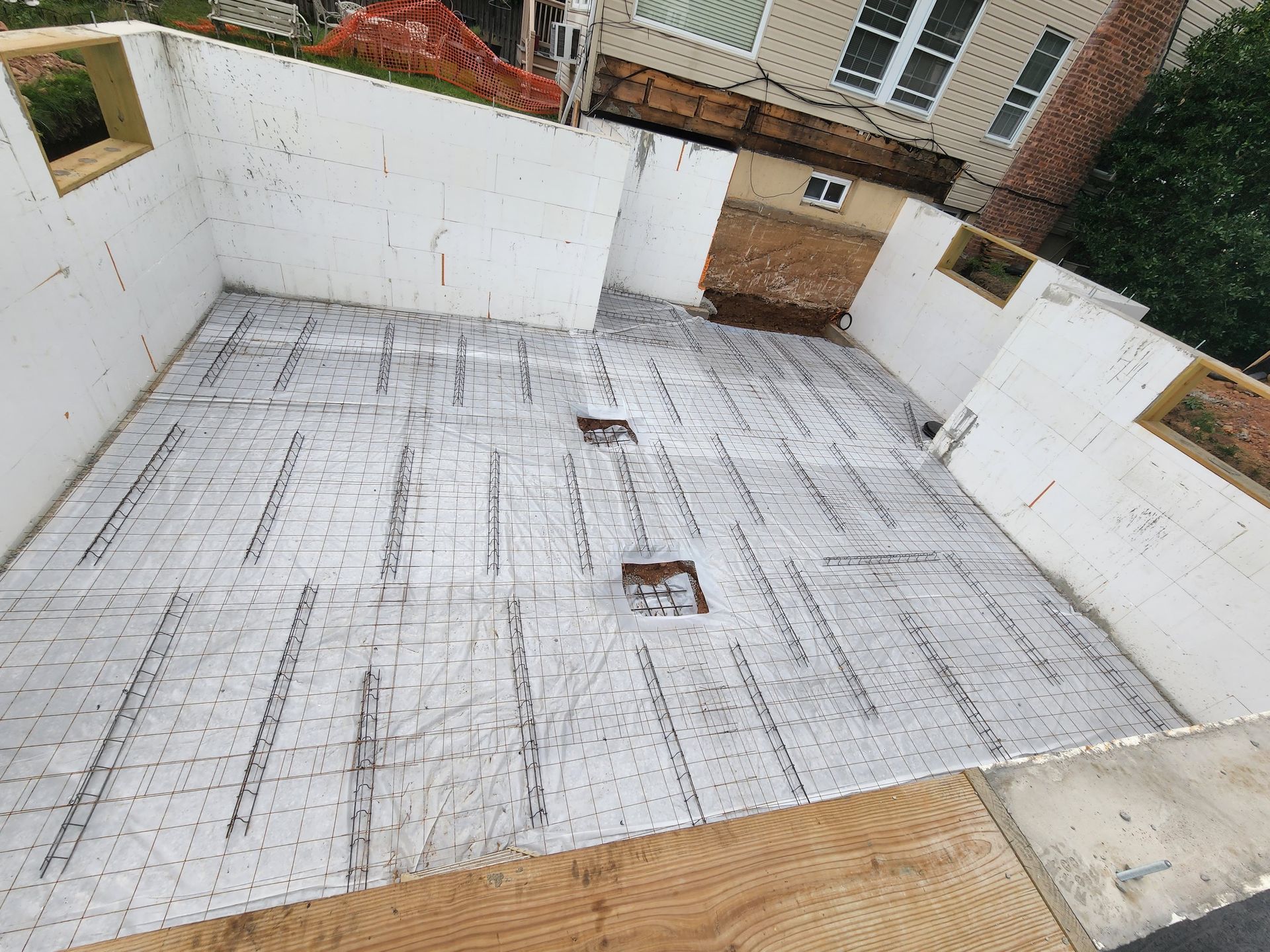 A construction site shows foam wall panels installed on a slab foundation with wire mesh laid out for a concrete pour.