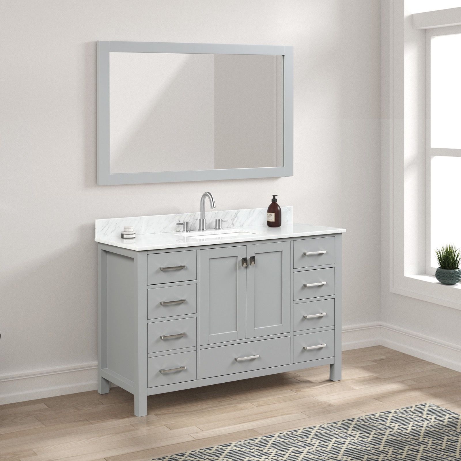A gray bathroom vanity with a white marble countertop, sink, and matching wall-mounted mirror in a room with wood floors.