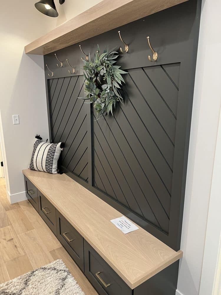 A charcoal entryway mudroom bench with natural wood top, diagonal wood paneling, hooks, and a decorative wreath.