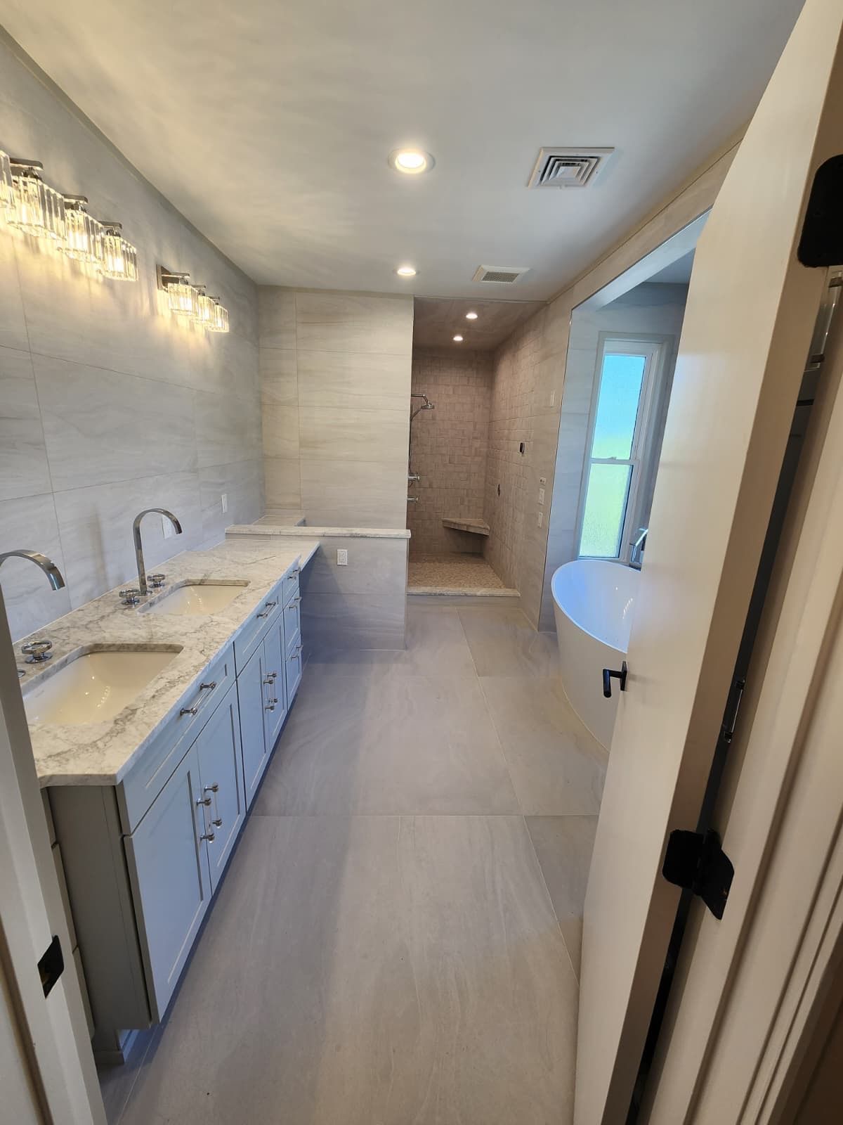 A modern bathroom with a double vanity, marble countertops, tiled floors, a walk-in shower, and a soaking tub.