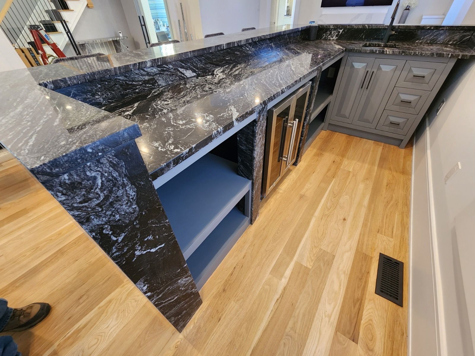 A high-angle view of a kitchen island with black marble-style countertops, grey cabinets, and light wood flooring.
