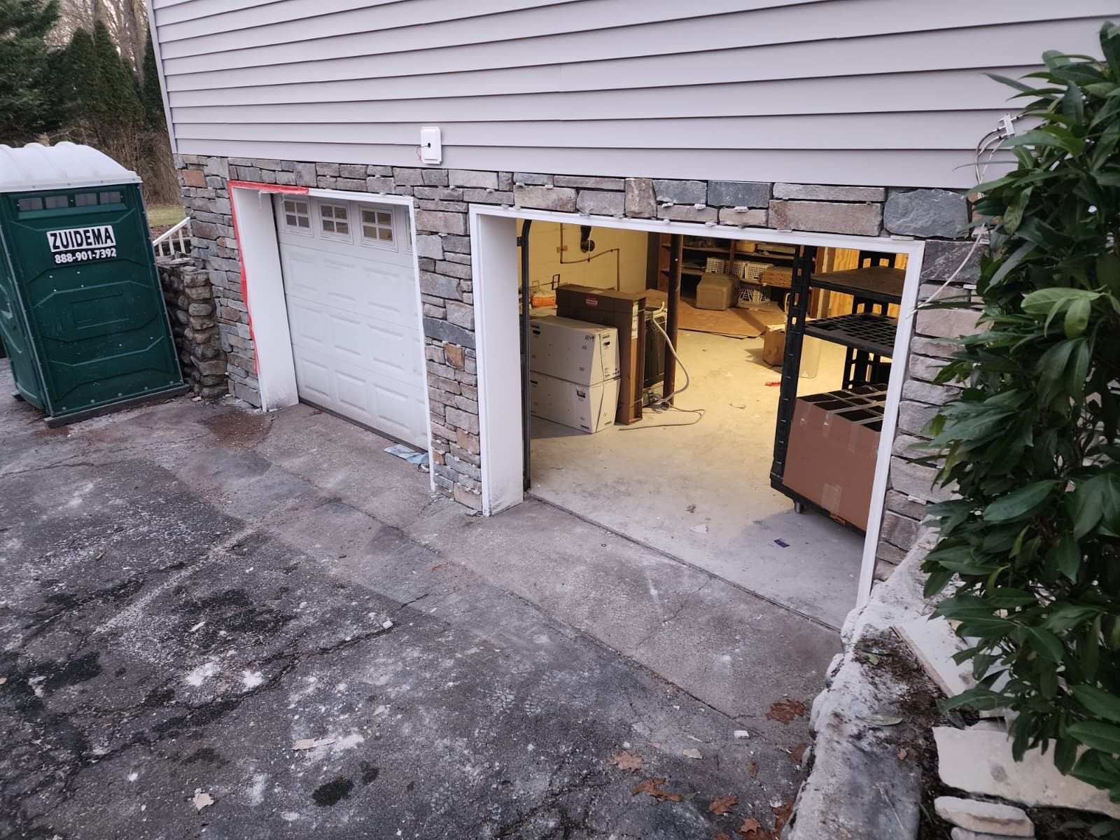 Two-car garage with stone veneer and one open bay, viewed from an outdoor driveway next to a portable toilet.