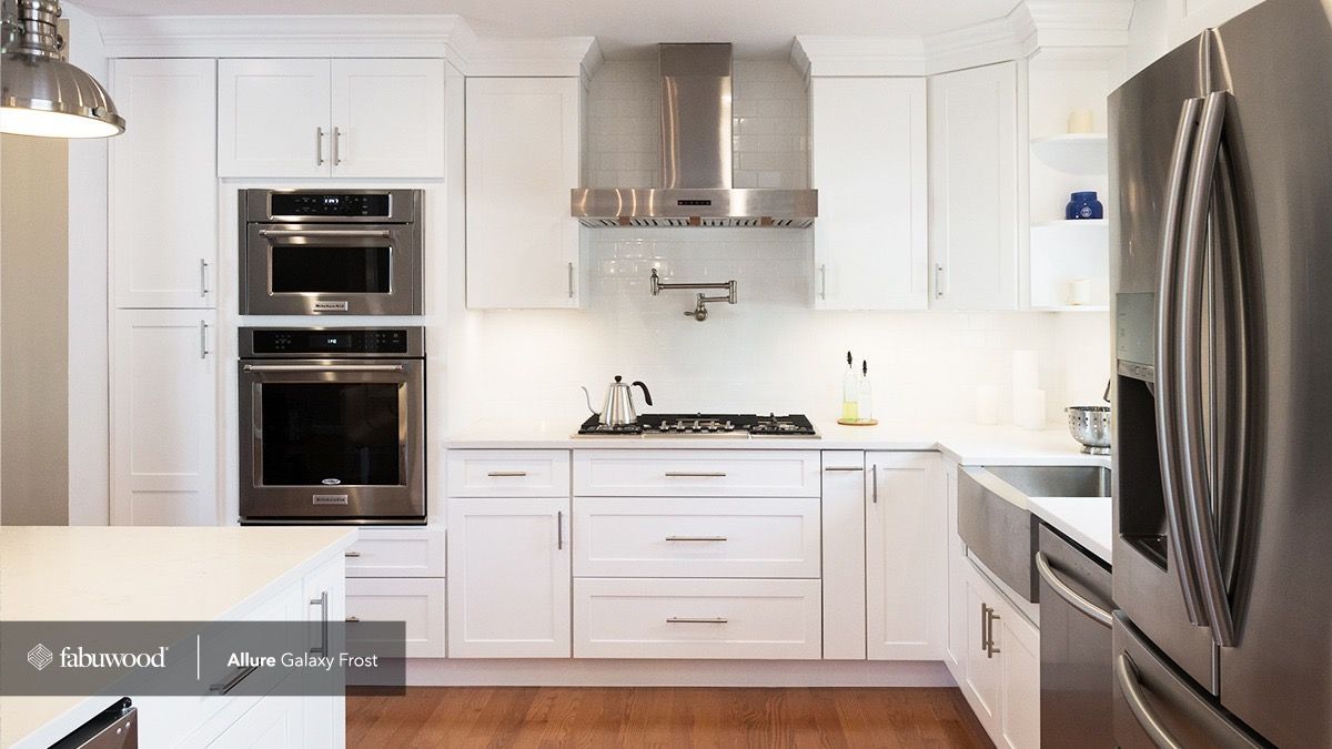 A bright kitchen with white cabinets, stainless steel appliances, a farmhouse sink, and a stovetop with a wall-mounted faucet.