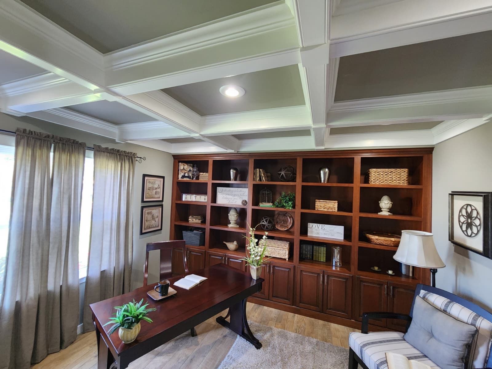 A home office featuring a dark wood desk, matching built-in bookshelves, beige curtains, and a coffered ceiling.