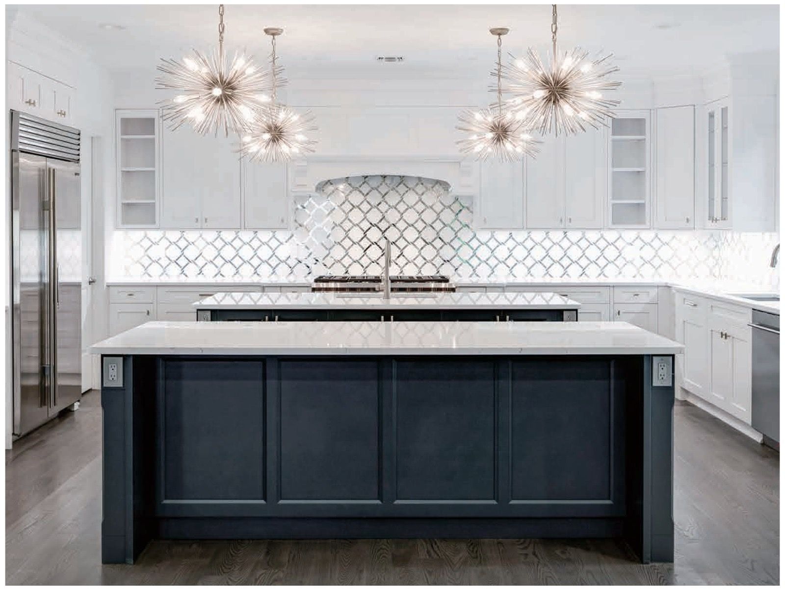 A bright, modern kitchen featuring a dark blue island with a white countertop and two ornate, starburst-style chandeliers.