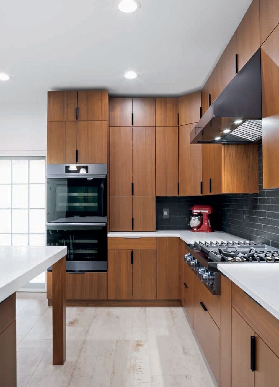 Modern kitchen with wood cabinets, white countertops, built-in double oven, gas range, and black tile backsplash.