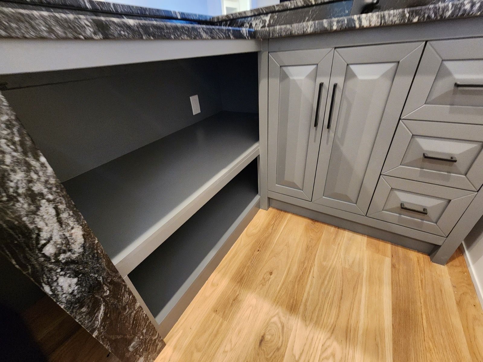 A corner kitchen cabinet with open gray shelves on the left and gray paneled cabinet doors and drawers on the right.