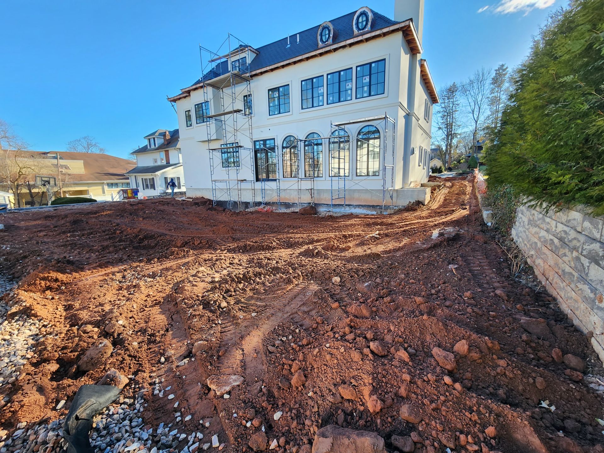 A large, multi-story house under construction with scaffolding against a freshly cleared, reddish-brown dirt yard.