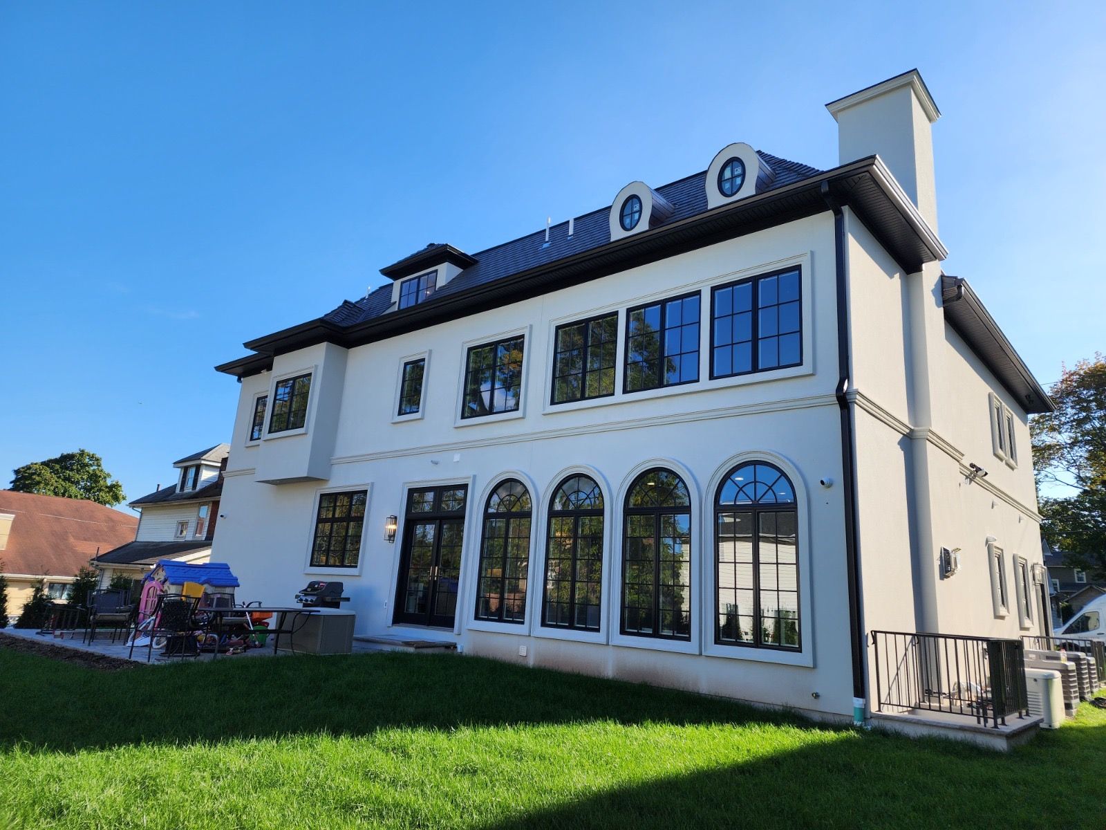 A large, two-story white stucco home with a dark roof and arched windows under a bright blue sky.
