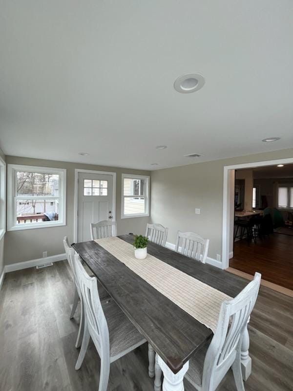 A dining room with a long, dark wood table, white chairs, a beige table runner, and light wood flooring.