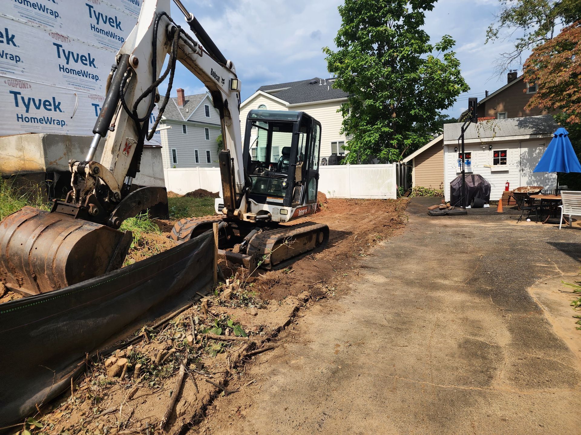 A white Bobcat excavator sits in a construction area next to a building wrapped in Tyvek house wrap.