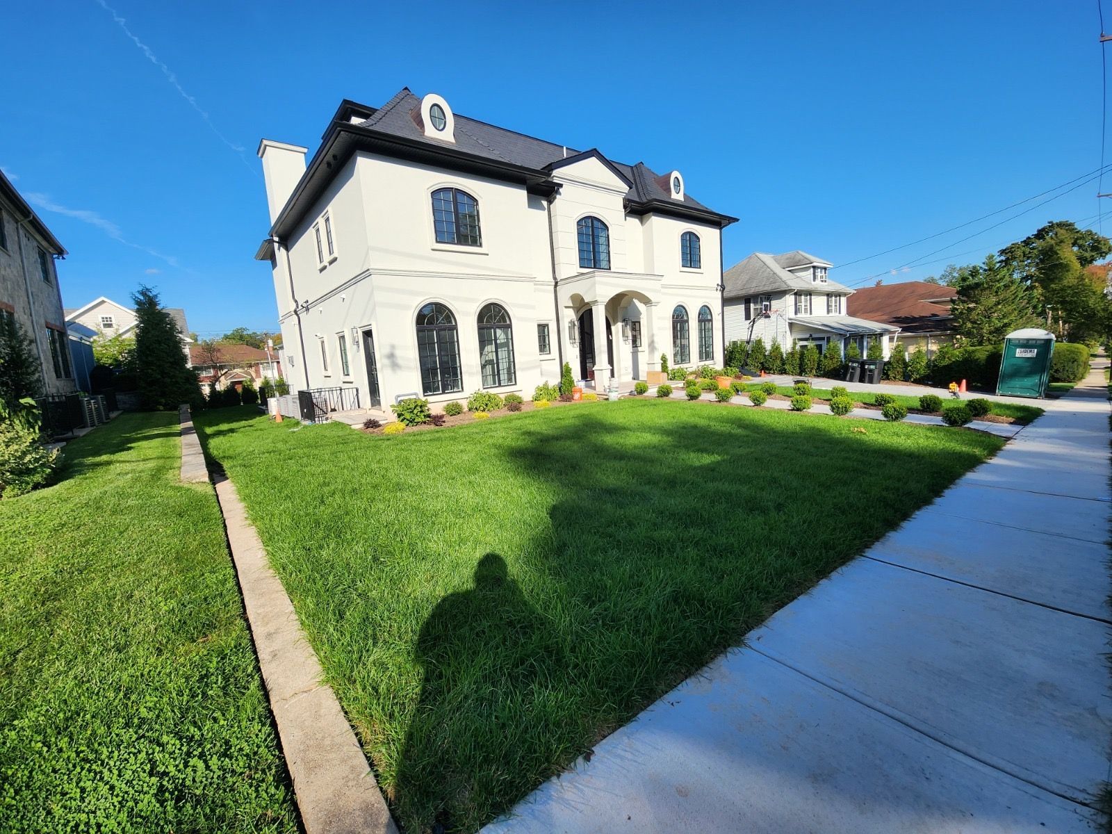 A large, two-story white house with a dark roof and manicured lawn under a clear blue sky.