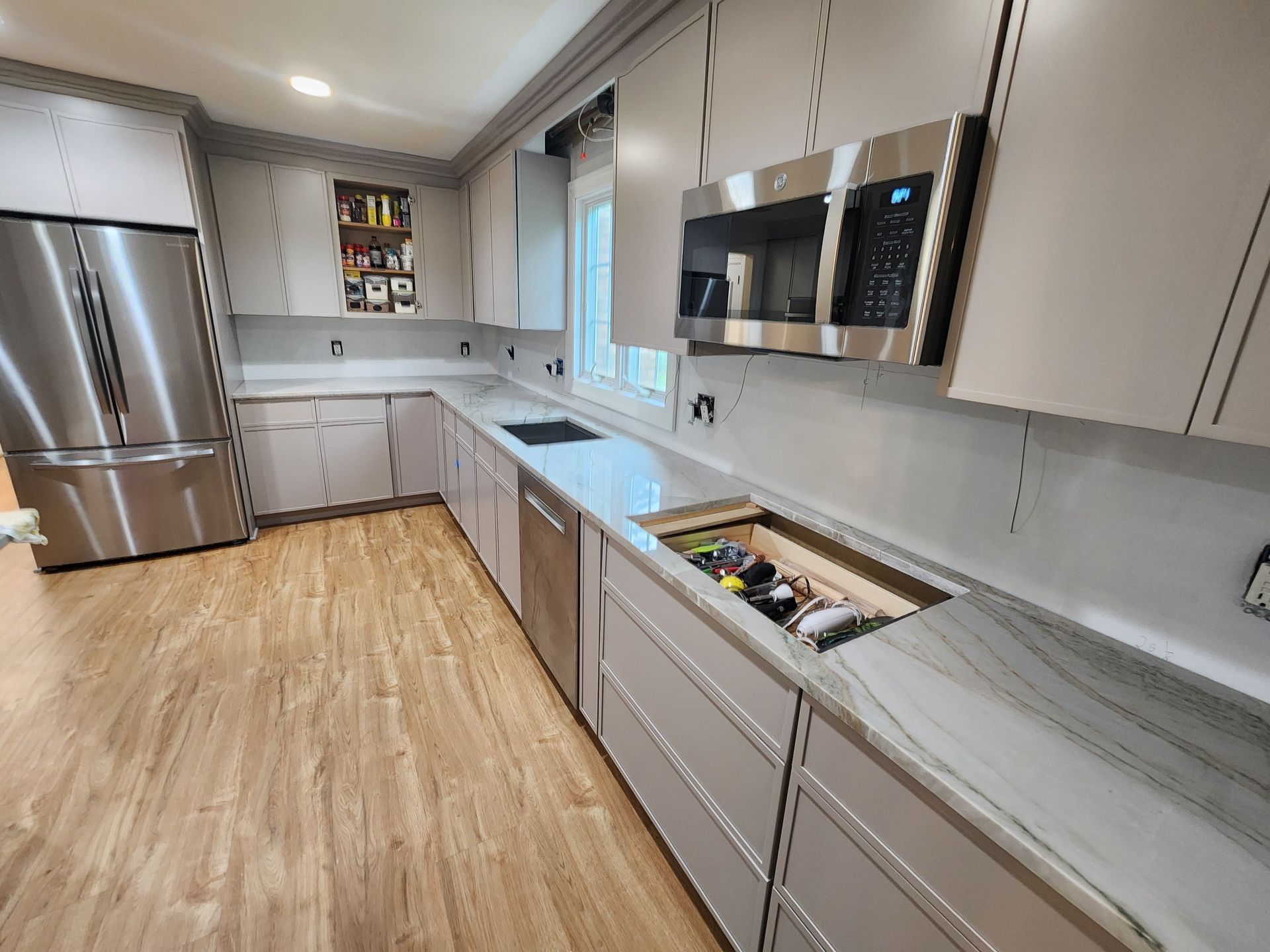 A modern kitchen featuring light grey cabinets, stainless steel appliances, light wood floors, and marble-style countertops.
