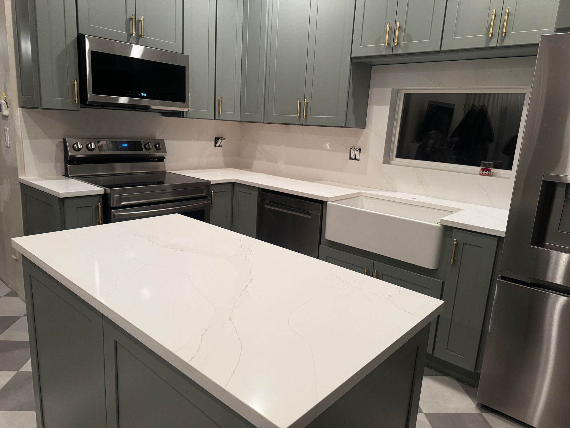 Modern kitchen with sage green cabinets, white marble-patterned countertops, stainless steel appliances, and tiled floors.