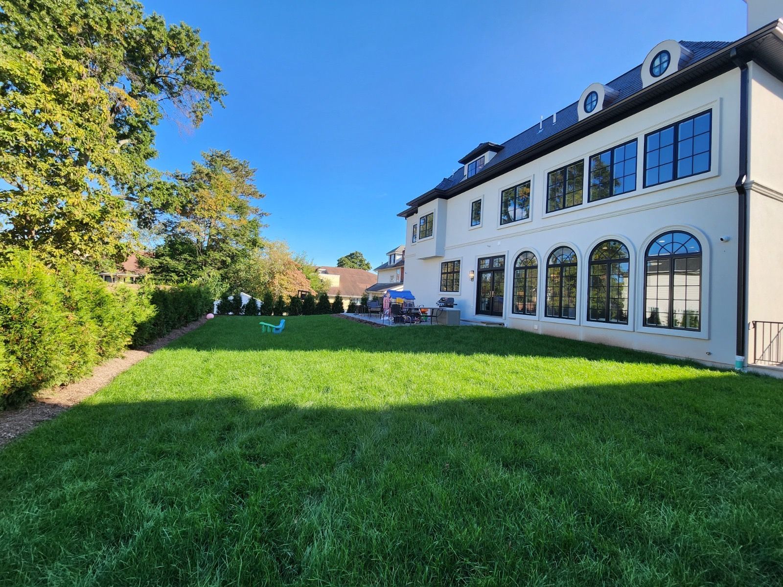 A large, white, multi-story building with arched windows stands beside a vibrant green lawn under a clear blue sky.