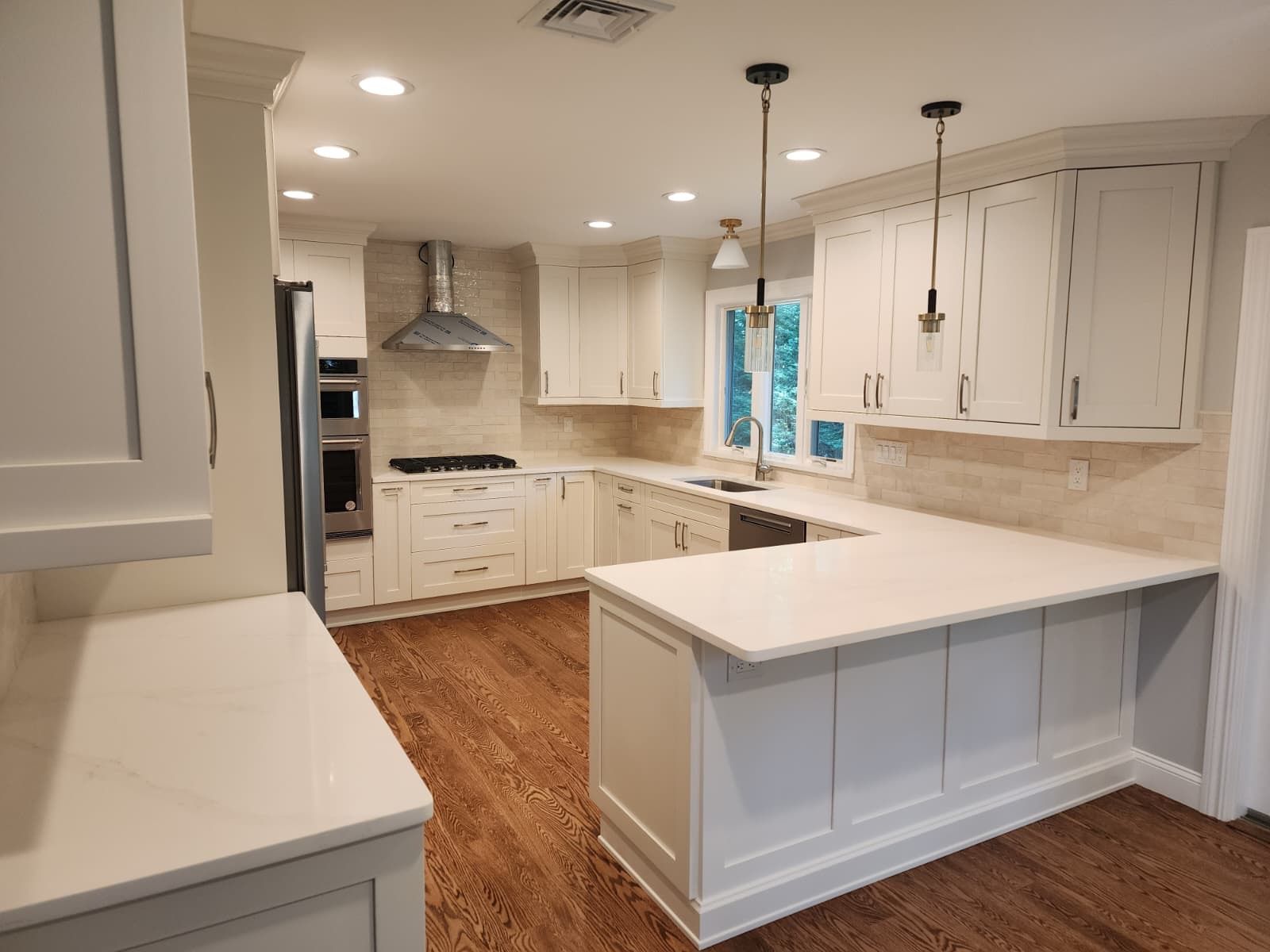 A bright kitchen with white cabinets, light-colored countertops, hardwood floors, and stainless steel appliances.