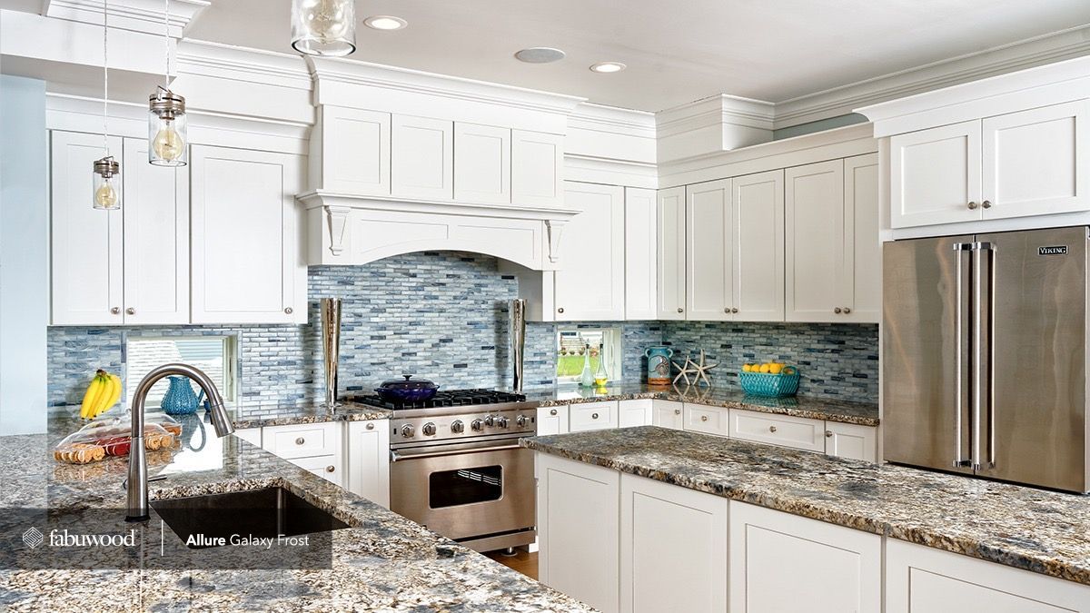 A modern kitchen with white shaker cabinets, granite countertops, blue mosaic tile backsplash, and stainless appliances.