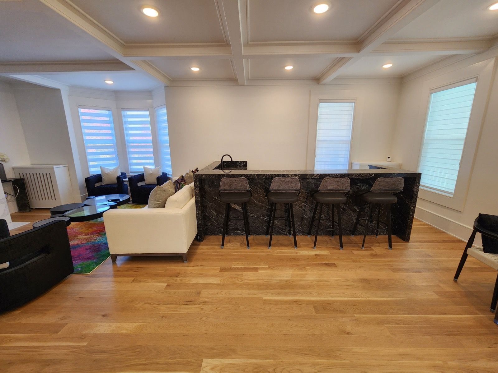 A spacious room with light wood floors, a white sofa, and a black marble kitchen island with four matching bar stools.
