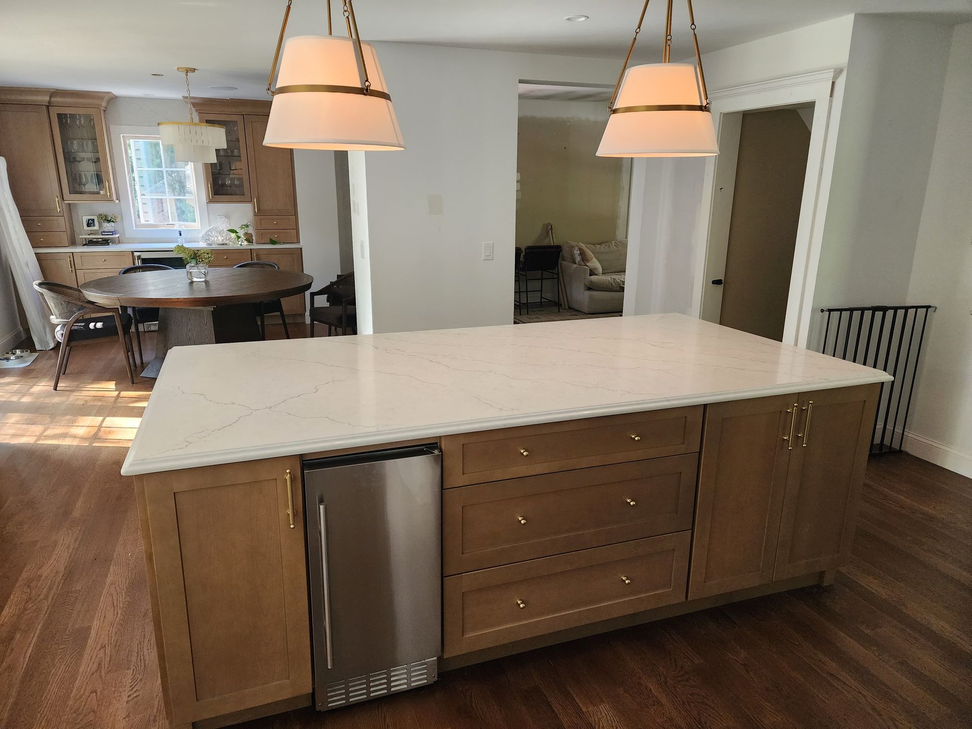 A kitchen island with light wood cabinets and white countertops, featuring a built-in stainless steel beverage fridge.