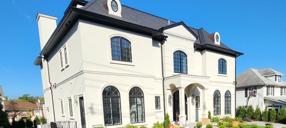 Large white two-story house with black roof and arched windows under a clear blue sky.