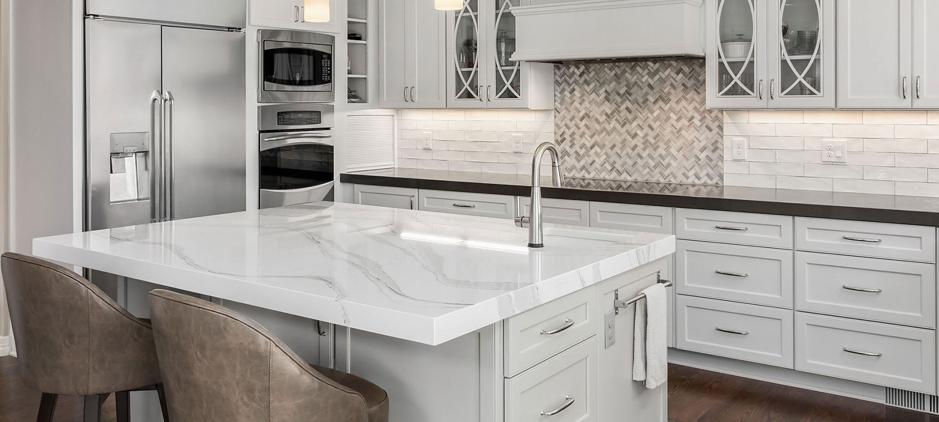 A modern, bright kitchen with a large white marble island, stainless steel appliances, and white cabinetry.