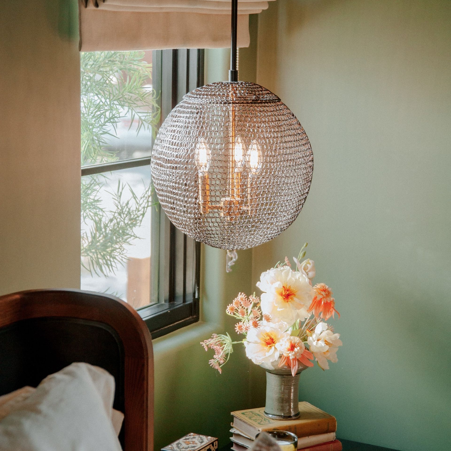 A bedroom with a lamp hanging from the ceiling and a vase of flowers on a nightstand