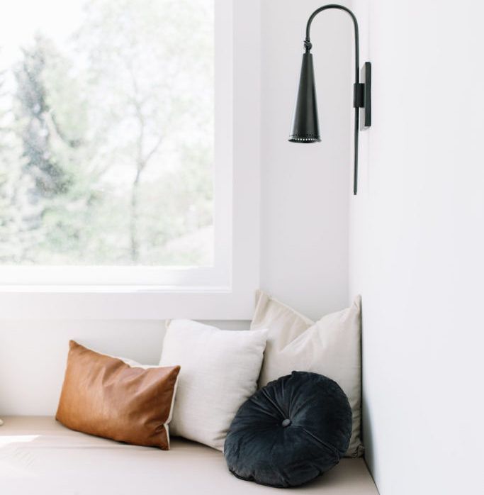 A window seat with pillows and a lamp on the wall