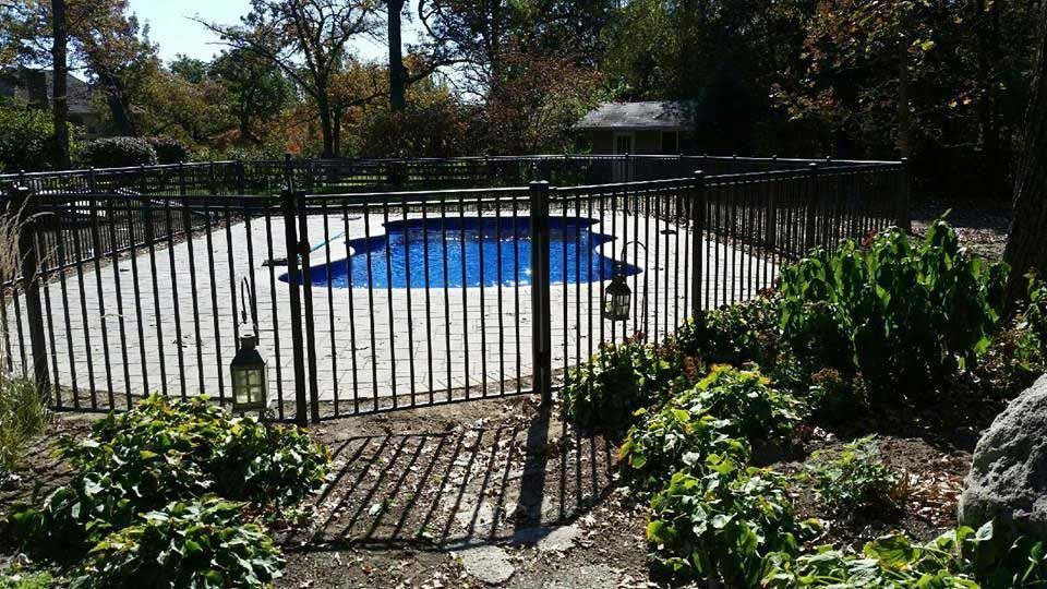 A fence surrounds a large swimming pool in a backyard.