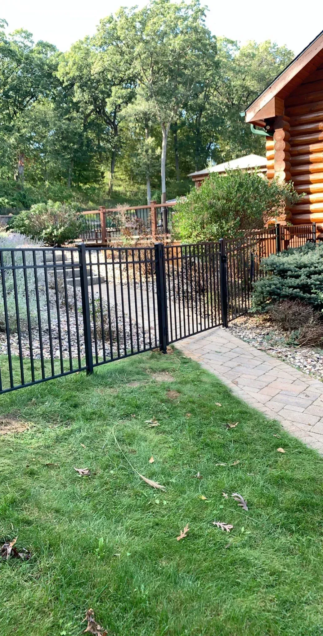 A wrought iron fence surrounds a lush green yard in front of a log cabin.