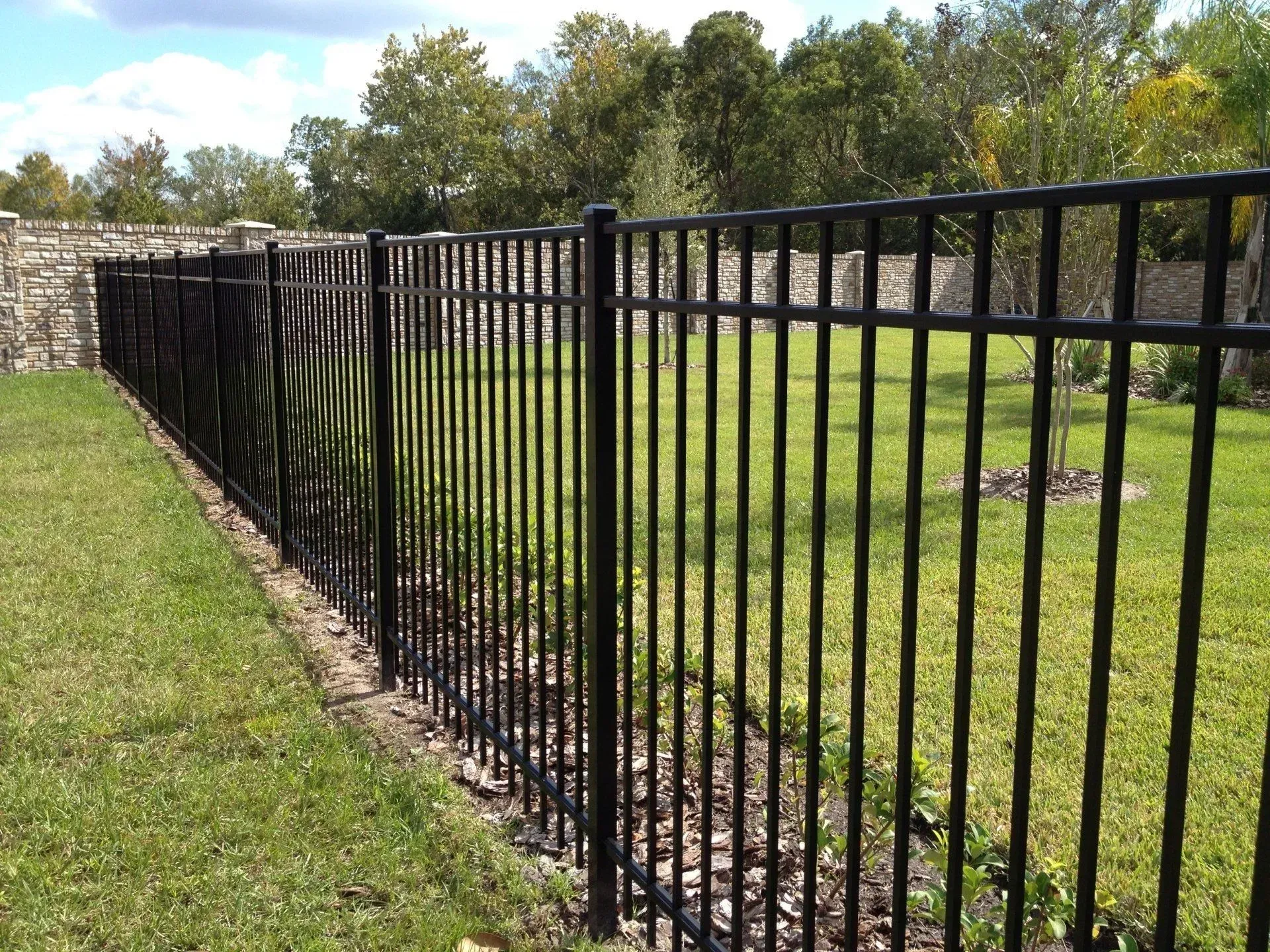 A black metal fence surrounds a lush green field