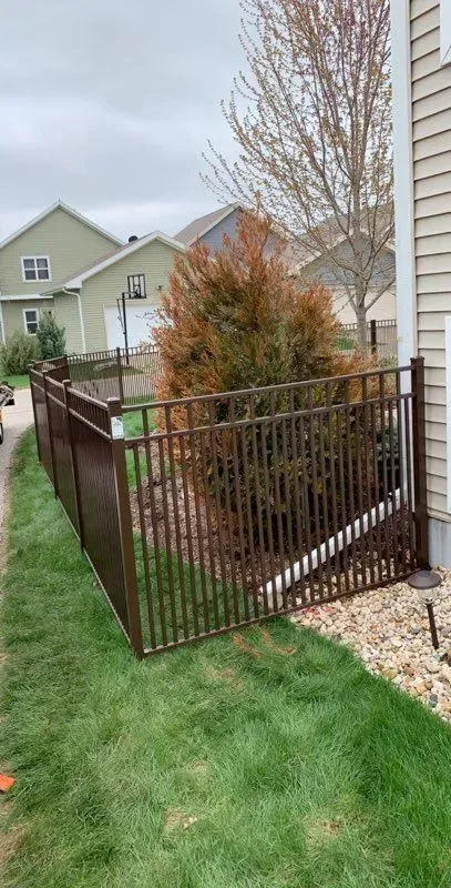 A metal fence surrounds a lush green yard next to a house.