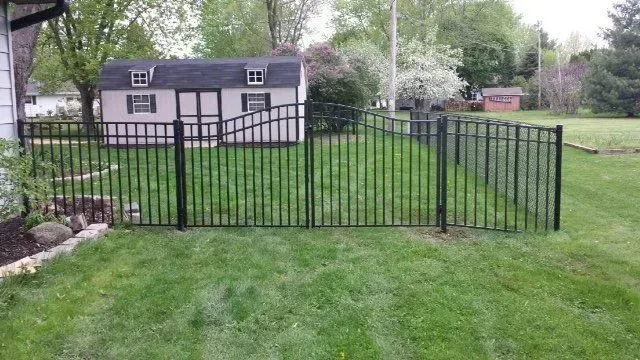A black fence surrounds a lush green yard in front of a house.