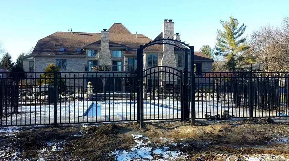 A large house is behind a fence with a gate in front of it.