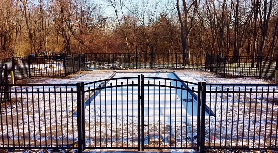 A black fence surrounds a swimming pool in the snow.