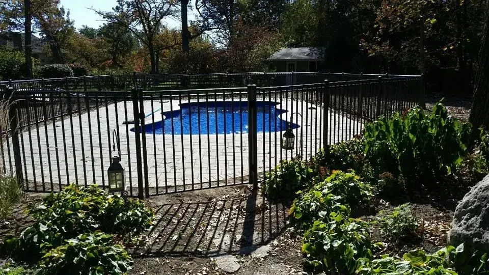 A fence surrounds a swimming pool in a backyard.