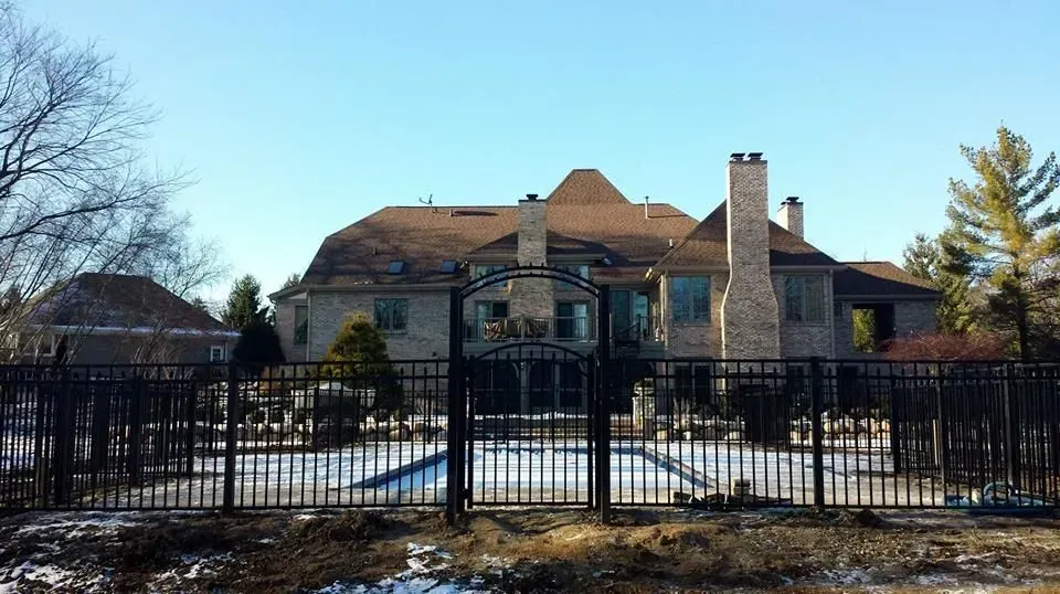 A large house with a fence around it and a pool in front of it.