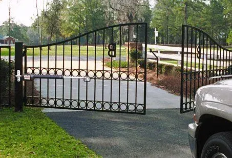 A car is parked in front of a wrought iron gate that is open.