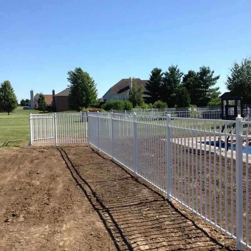 A white fence surrounds a swimming pool with a house in the background