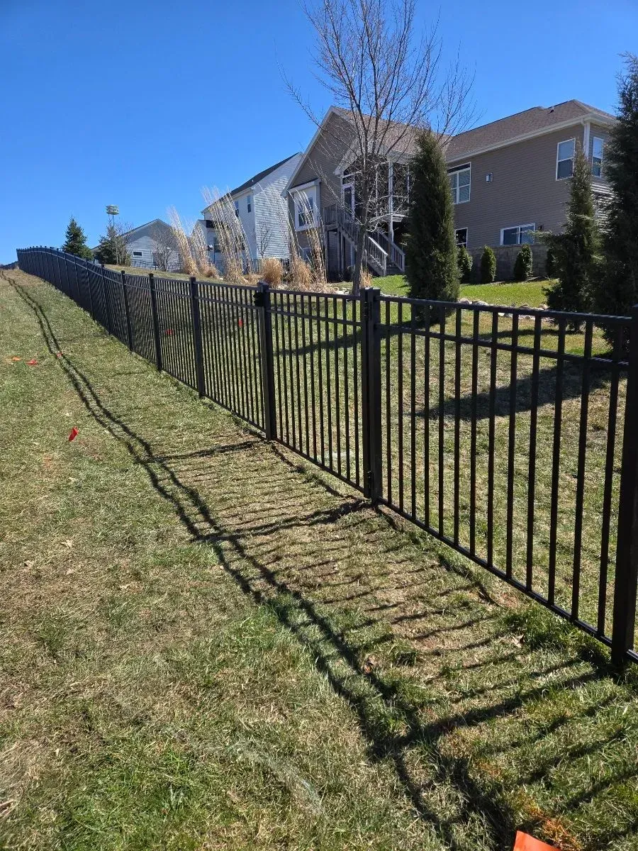 A black metal fence surrounds a grassy yard in front of a house.